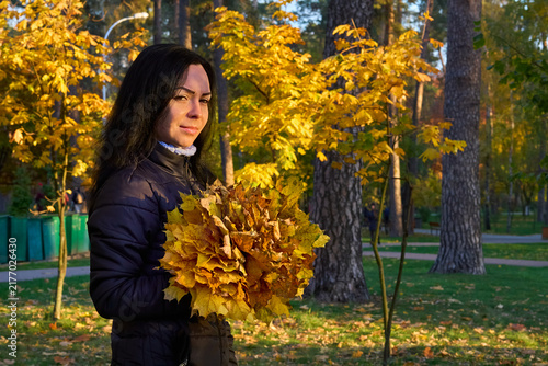Cute young woman with bouquet of autumn leaves is walking in forest park