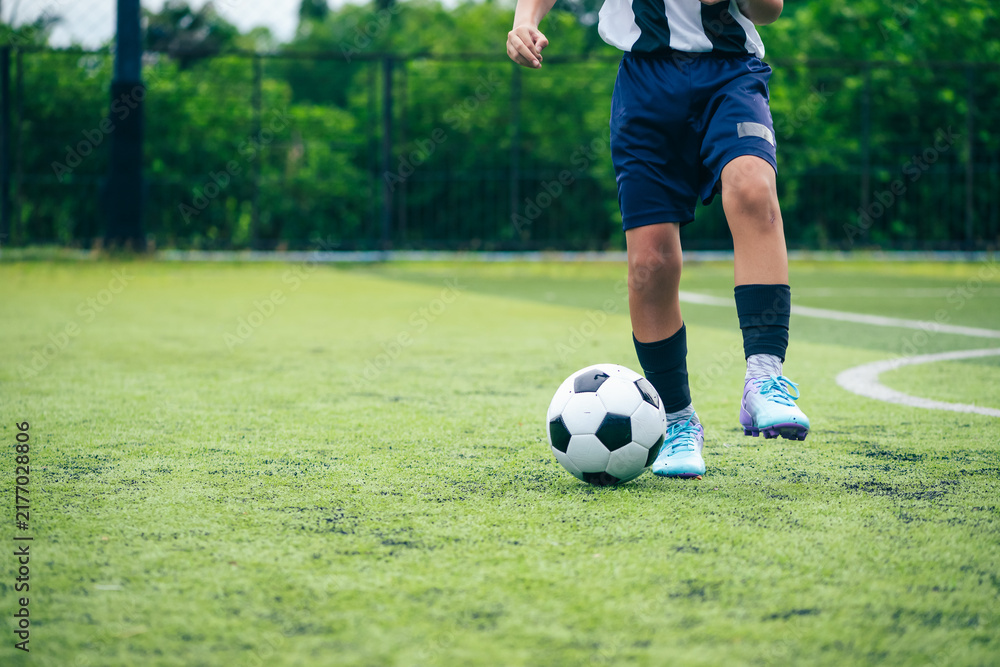 Obraz premium Kid boy leg kicking soccer ball on green grass field action. conceptual metaphor for youth sports training team competition fitness health wellness and active lifestyle 