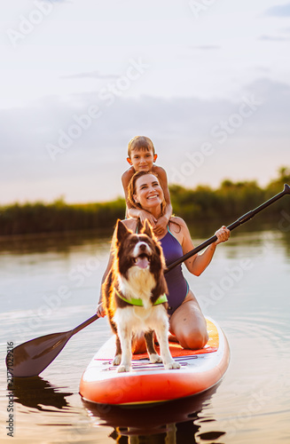Happy mother and son paddleboarding on river with thair dog on board.
