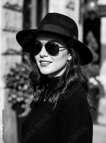 Black-and-white portrait of an elegant woman wearing a fedora and sunglasses.