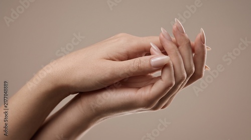 Elegant female hands featuring long almond shaped manicured nails with glossy beige polish presented in a soft studio lighting setup for beauty and skincare advertising photography