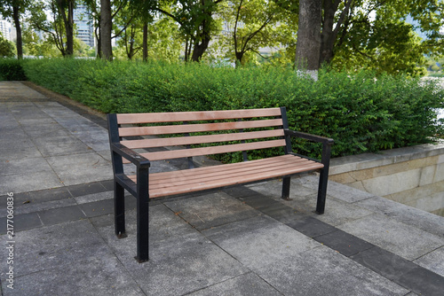 Cuadro en lienzo Empty park bench along a paved walkway with lush green bushes