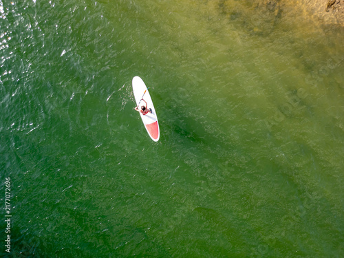 Woman paddle surf on green lake water from above