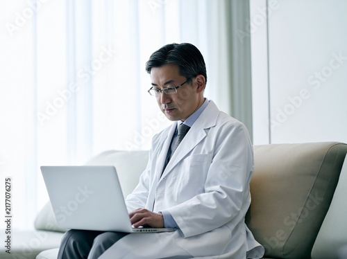 ソファに腰掛けリラックスしながらもPC作業に集中する男性医師