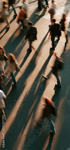 People moving across urban pedestrian crossing with motion blur. Busy crowd walking on crosswalk, creating dynamic flow and long shadows