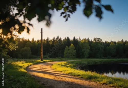 Sunlit dirt path winding through lush green meadow toward serene lake and dense forest