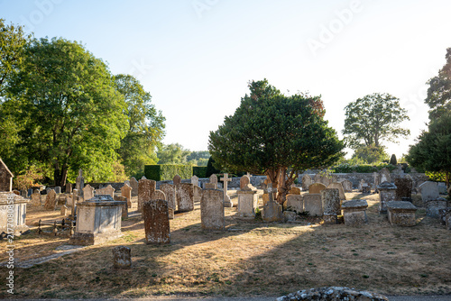 Foto Old churchyard filled with ancient gravestones, stone tombs, and mature green trees in bright sunlight