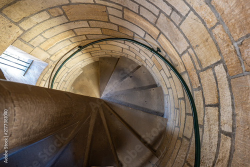 фотографія Looking down a winding stone spiral staircase inside a historic tower with a metal handrail and stone wall