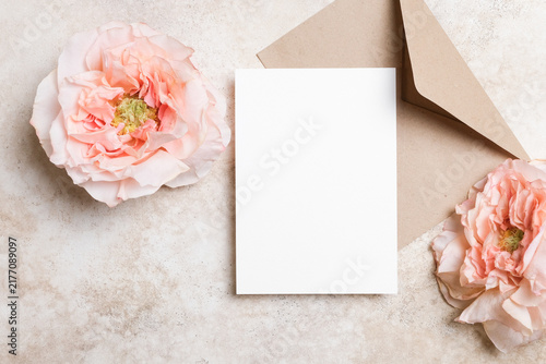 Blank white wedding card mockup on a beige background with envelope and rose flower. Elegant and minimalist flat lay for invitation or greeting card design