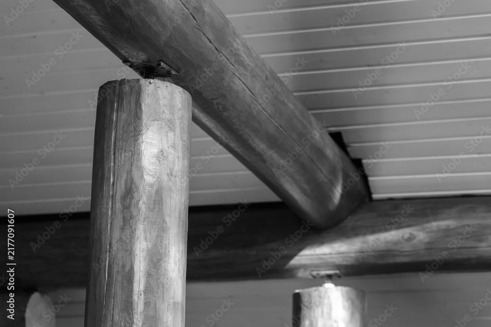 Obraz premium Monochrome close-up of rustic wooden beams and round log columns supporting a paneled ceiling, highlighting timber grain, joinery and texture in an interior architectural study