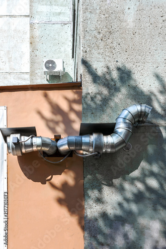 The metal ventilation pipe and fan are installed on the building wall.