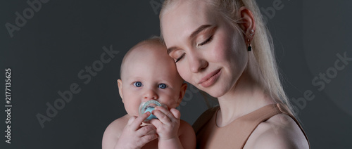 Bild auf Leinwand Young caucasian mother tenderly holding her baby boy with a pacifier in a wide s
