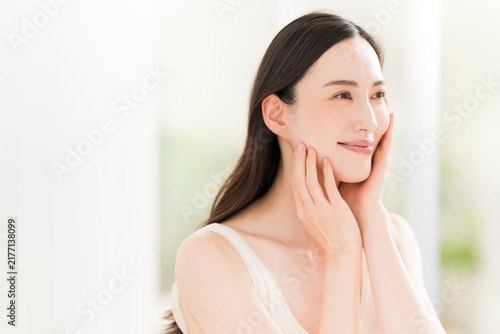 顔を触る笑顔の日本人女性。スキンケアイメージ。