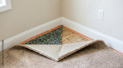 Carpet folded back in room corner revealing foam padding underlay and wooden subfloor boards