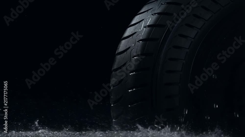 Vehicle Tire Rolling Through Shallow Water With Dramatic Splashes in a Dark Setting