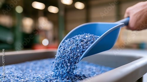 Industrial worker pour blue plastic regrind from scoop in manufacturing facility, sustainable material processing and recycling plant scene