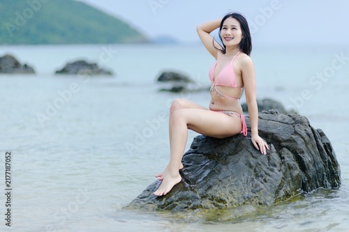 Woman in Pink Swimsuit Posing on Rock at Beach During Summer Day