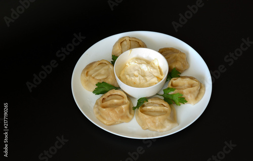 Obraz na płótnie Manti, traditional Asian dumplings steamed with parsley and sauce, in a round plate against a black background