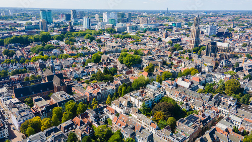 Aerial drone view of Utrecht, Netherlands featuring its historic church tower, red‑roofed buildings, modern skyline, and sunny urban landscape blending old and new architecture.