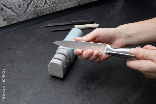 Person inspecting a sharpened stainless steel kitchen knife after completing the blade sharpening process. Concept of knife inspection, sharpness, kitchen maintenance, cooking equipment, home care.