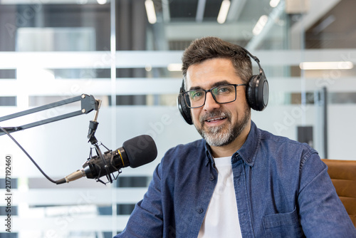 Фотография Man in glasses and headphones smiling while recording a podcast in a modern stud