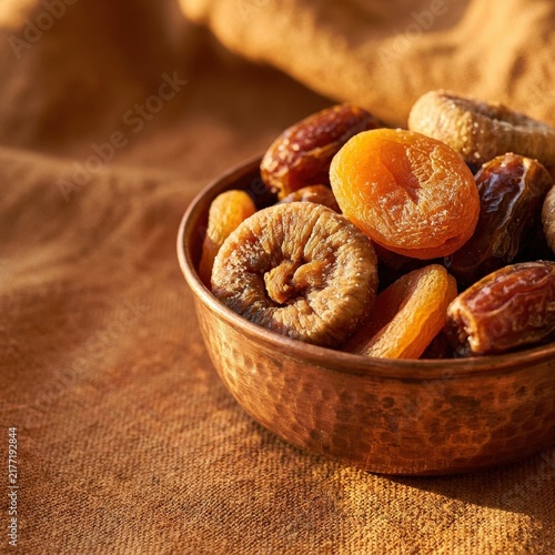 Assortment of healthy dried apricots, figs, and dates in a rustic copper bowl on a dark surface