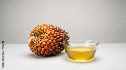 Fresh oil palm fruit bunch and a bowl of refined golden oil on a clean background.