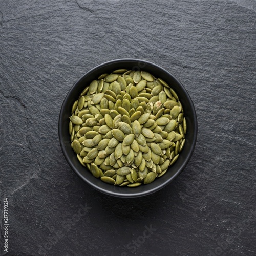 Fresh pepitas in a ceramic bowl on dark textured stone surface for healthy snacking