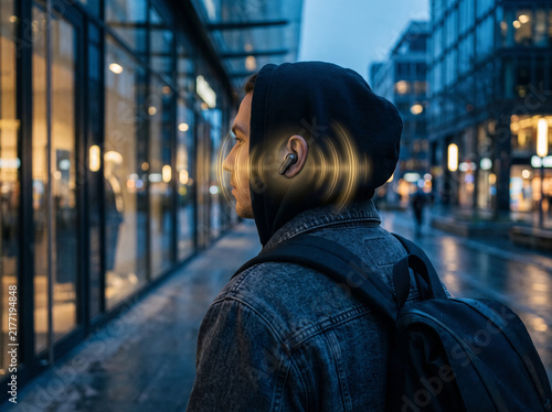 Man walking city street at night with glowing sound wave audio technology around his ear.