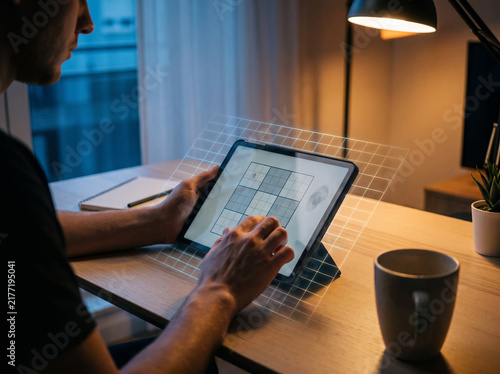Person using digital tablet for design work at cozy home office desk with lamp.
