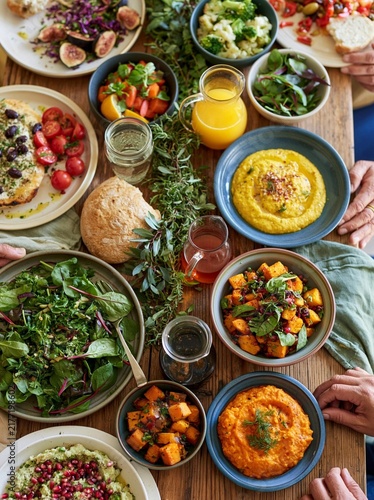 Group of people sitting around a wooden table with a variety of food and drinks. there are plates, bowls, and glasses of orange juice on the table.
