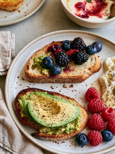 Plate with two slices of toast topped with avocado and fresh berries. the toast is golden brown and appears to be freshly baked.