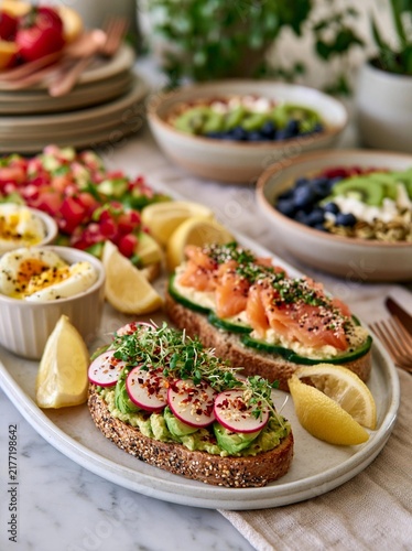 Plate of food on a table with a marble countertop. on the plate, there are two slices of bread topped with avocado, sliced radishes, and sprouts.