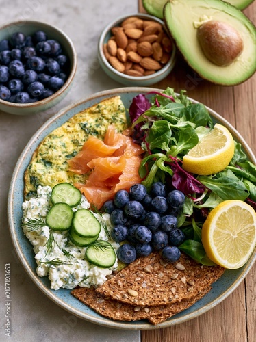 Plate of food on a wooden table. the plate is blue and has a variety of colorful ingredients on it.