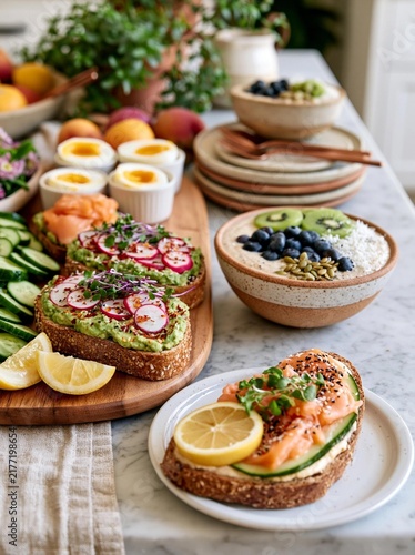 Table with a variety of food items on it. on the left side of the table, there is a wooden cutting board with three slices of bread topped with avocado, radishes, and salmon.