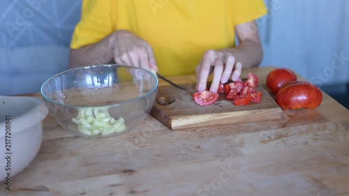 Woman's hands slicing fresh red tomatoes on wooden cutting board and putting them into glass bowl for vegetable salad