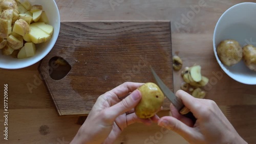 Person's hands cutting potatoes on wooden cutting board for meal preparation in kitchen, top down view