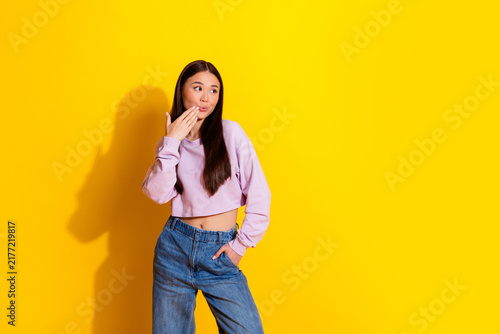Young woman in lilac cropped sweatshirt and jeans posing surprised against a bright yellow background