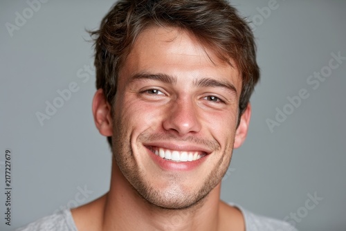 Portrait of a smiling young man with a bright, whiter smile against a neutral grey background
