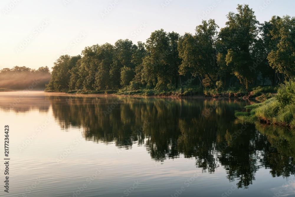 Obraz premium Serene river landscape with reflected trees and soft sky