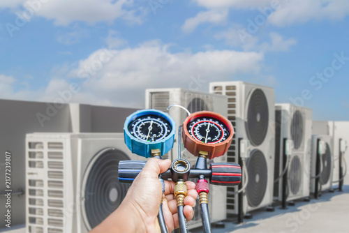 Air conditioning, HVAC service technician using gauges to check refrigerant and add refrigerant.