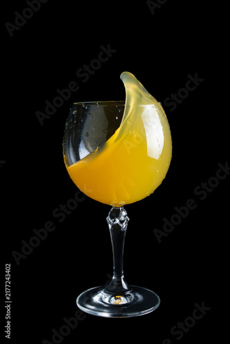 Bright yellow drink splashes in a glass with a dark background at a party event