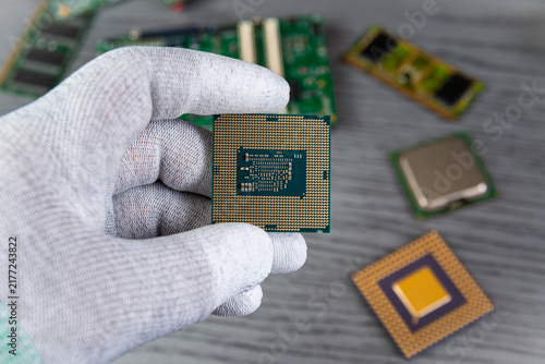 Hand holds a computer chip among other electronic parts on a gray surface