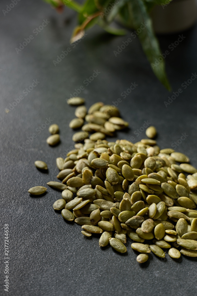 Obraz premium Pumpkin seeds are scattered on a dark surface with a plant in the background