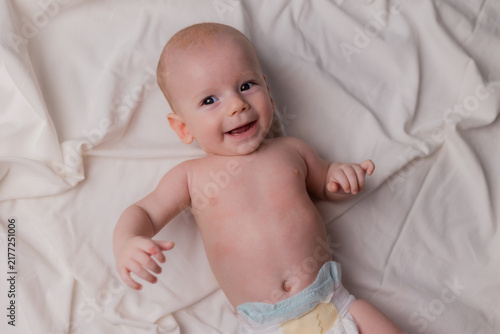 4‑month‑old baby in diapers is lying on the bed, viewed from above. Portrait of the baby against a light background.