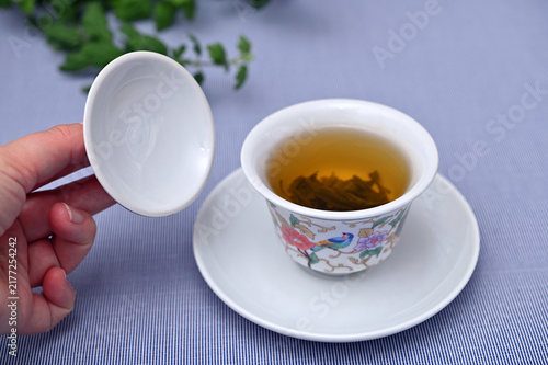 Hand holding lid of Chinese porcelain gaiwan bowl filled with freshly brewed green tea