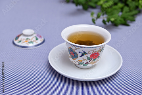 Fresh green tea in traditional Chinese porcelain gaiwan bowl on blue background