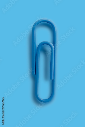 Close-up view of a single blue paperclip on a green textured background. Monochromatic minimalist composition emphasizes simplicity and everyday stationery.