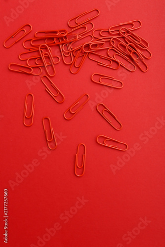 Scattered Red Paperclips on Red Background. Minimalist photo of red paperclips scattered randomly across a red surface. Monochromatic composition emphasizes repetition, texture, and stationery design.