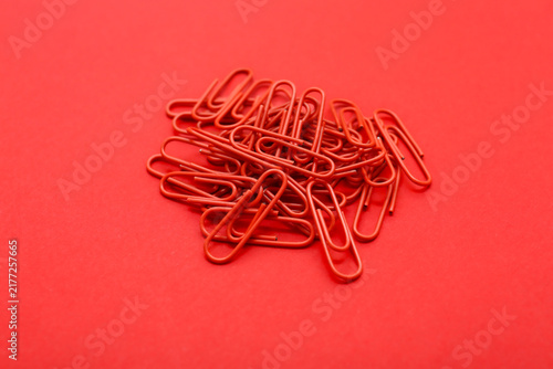 Monochromatic photo of multiple red paperclips piled together on a red surface. Minimalist composition emphasizes texture, stationery, and everyday objects.